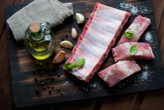 Raw pork ribs with seasonings on a dark rustic wooden surface