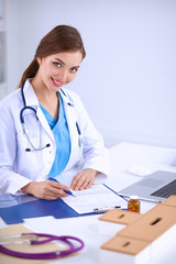 Beautiful young smiling female doctor sitting at the desk and writing