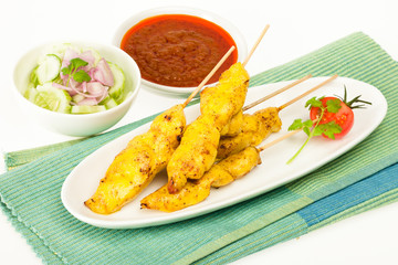 Chicken grilled meat on sticks with cucumber salad on side and chilli sauce