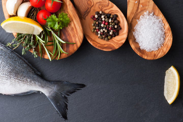 fresh raw dorado fish with spices and herbs on black background, top view