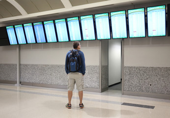 Man is looking and pointing at a departure/arrival board at an airport