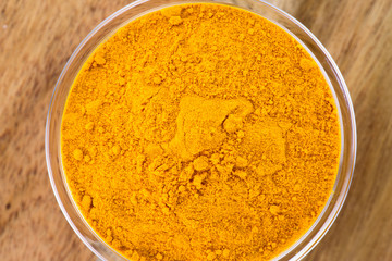 The powder of turmeric in the glass bowl on the wooden background.