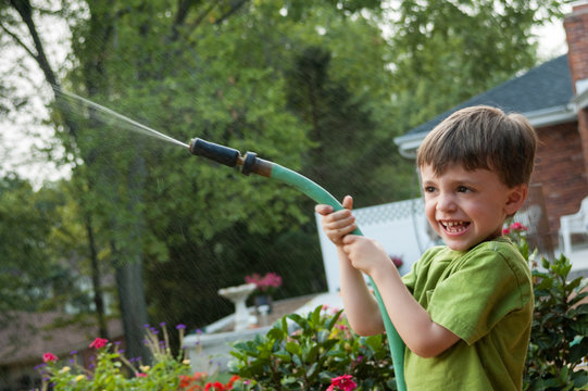 Child Watering Garden With Hose