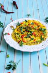 Delicious breakfast omelette or scrambled eggs with red and yellow tomatoes, red hot chili peppers and parsley on patterned plate over stylized old aged turquoise table background close-up, copy space