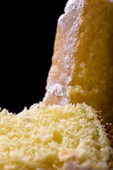 pandoro cake and slice with icing sugar on black background