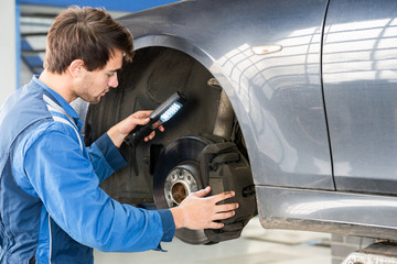 Mechanic Examining Brake Disc Of Car In Garage - 95347557