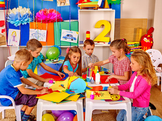 Kids holding colored paper and glue on table in kindergarten .