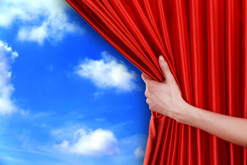 Human hand opens red curtain on sky background