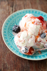 Delicious ice cream with fresh frozen berries and sauce, on wooden background