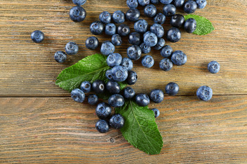 Tasty ripe blueberries with green leaves on wooden table close up