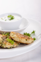 Cabbage pancakes with parsley and yogurt dressing on a white plate. Top view.