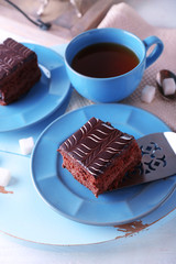 Served table with a cup of tea and chocolate cakes on blue plates close-up