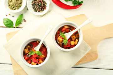 Tasty vegetarian ratatouille made of eggplants, squash, tomatoes in bowls on wooden table background