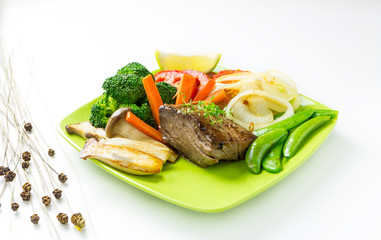 Tasty fish steak with grilled vegetable on plate isolated on whi
