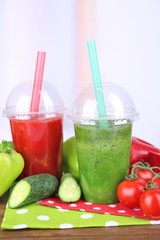Fresh vegetable juices in plastic cups on wooden table, on light background