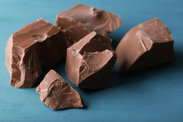 Milk chocolate pieces on color wooden background