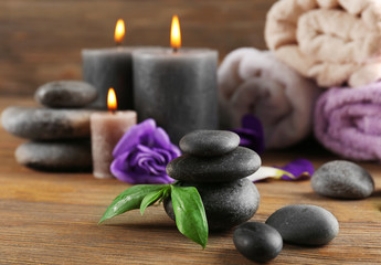 Fototapeta na wymiar Alight wax grey candles with flowers, towels and pebbles on wooden background - relax set