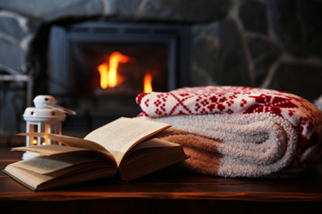 Hot tea or coffee in mug, book and candles on vintage wood table. Fireplace as background