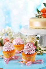 Tasty cupcakes and cake, on table, on light background
