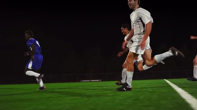 The camera pans with a soccer team as they score a goal, in slow motion
