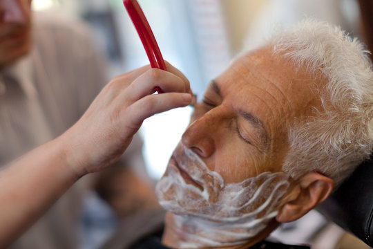 Senior man getting a shave in a barbershop. Selective focus on the customer.