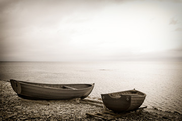 Two rowboats on a rocky beach at the edge of the sea. Dreamy moody toned image with copy space.