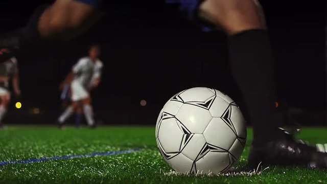 Close up of a soccer ball being kicked in slow motion at night
