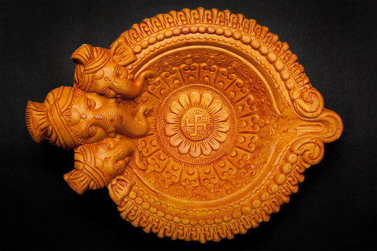 Top view of a beautifully carved designer handmade clay lamp with face of lord Ganesha on dark background.