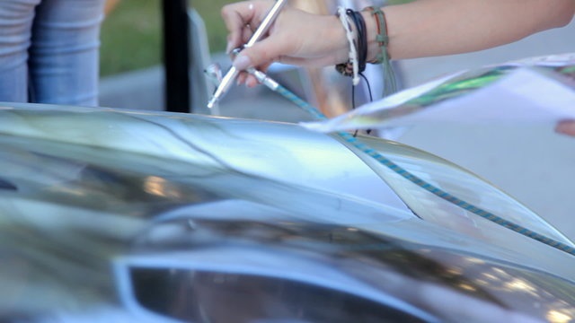 Footage of a car being painted with airbrush outdoors