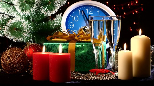 Glasses with champagne on New Year Eve against wall clock, candles, presents, bokeh, garland, on black, cam moves to the right