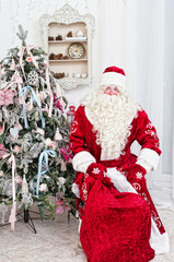 Obraz premium Saint Nicolas with a bag of gifts sits near a Christmas fir-tree
