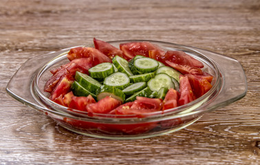 Tomato and cucumber  salad on the glass bowl on wooden background