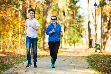 Obraz premium Teenage girl and boy running in city park 