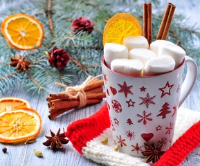 Obraz na płótnie Canvas chocolate or cocoa drink with marshmallows and cinnamon in a Christmas cup on the background of blue spruce