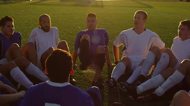 A soccer team sitting in a circle playing a fun game at sunset
