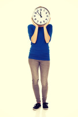 Young woman hiding behind a clock.