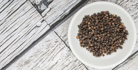Black peppercorn in white bowl over wooden background