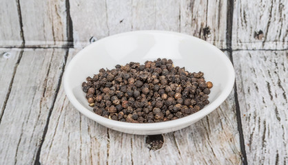 Black peppercorn in white bowl over wooden background