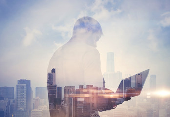 Double exposure of man with laptop and contemporary city on the background. Horizontal