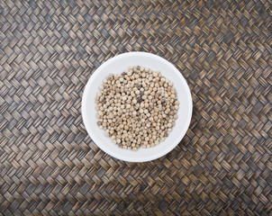 White peppercorn in white bowl over wicker background