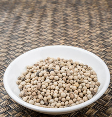 White peppercorn in white bowl over wicker background