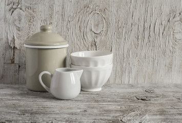 Fototapeta na wymiar Vintage crockery - enamel jug and white ceramic bowl on bright wooden surface. Rustic style