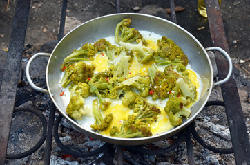 Fried eggs with broccoli, cooked in a large frying pan over a campfire