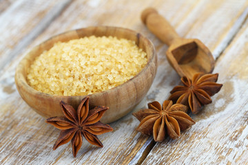 Brown sugar in wooden bowl and star anise on rustic wooden surface
