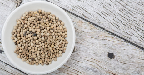White peppercorn in white bowl over wooden background