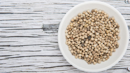 White peppercorn in white bowl over wooden background