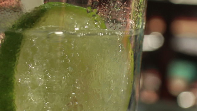 Macro CU tonic with lime while person splashes into a pool in the background
