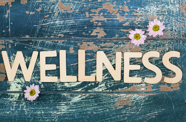 Wellness written on rustic wooden surface and pink daisy flowers
