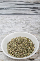 Dried lemon balm leaves in white bowl over wooden background