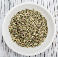Dried lemon balm leaves in white bowl over wooden background